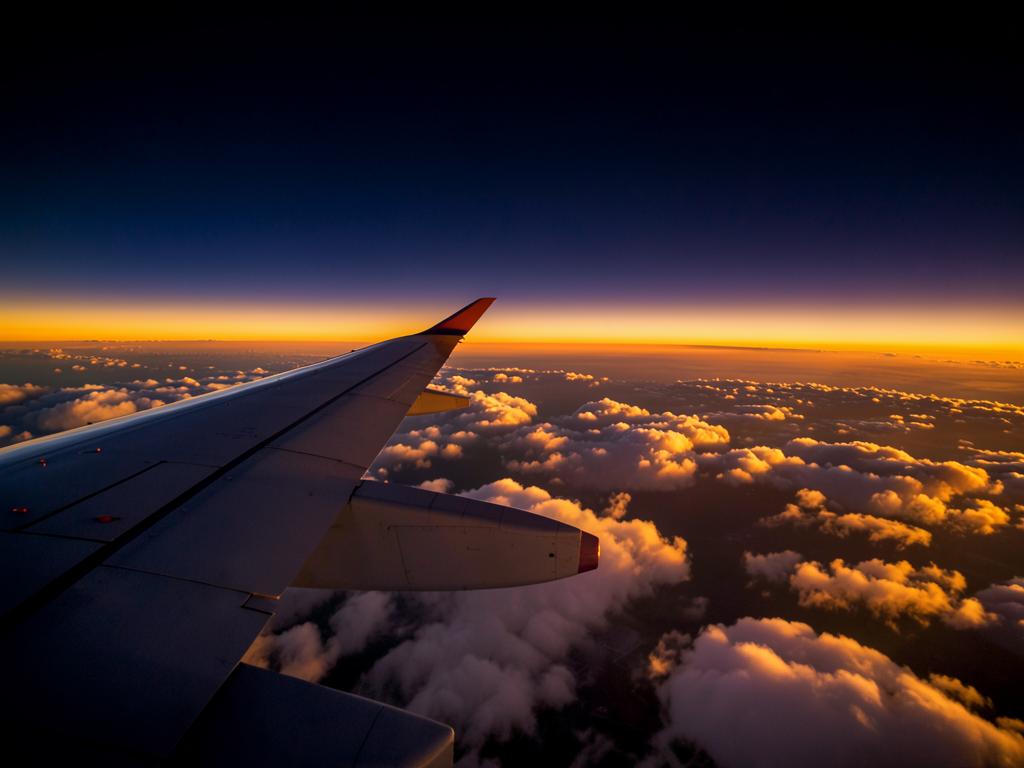 Asa de avião acima das nuvens ao pôr do sol